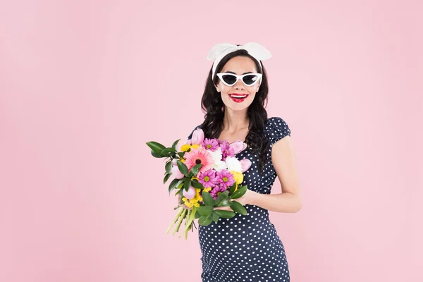 Чарівна вагітна жінка в сонцезахисних окулярах тримає квітковий букет ізольовано на рожевому — стокове фото
