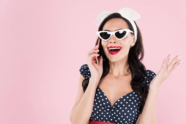 Приваблива брюнетка в сонцезахисних окулярах говорить на смартфоні ізольовано на рожевому — стокове фото