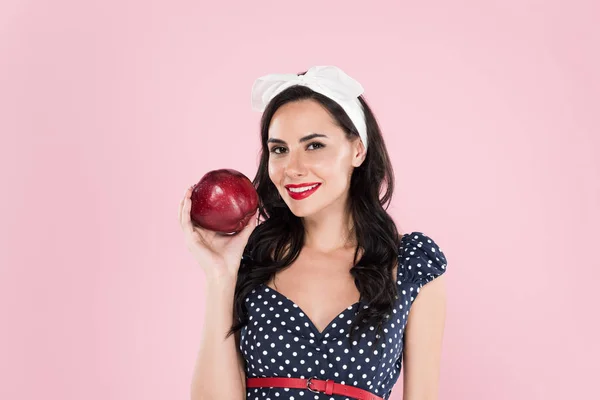 Stylish brunette woman in polka-dot dress holding ripe red apple isolated on pink — Stock Photo