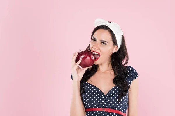 Wunderschöne brünette Mädchen in gepunktetem Kleid essen roten Apfel isoliert auf rosa — Stockfoto