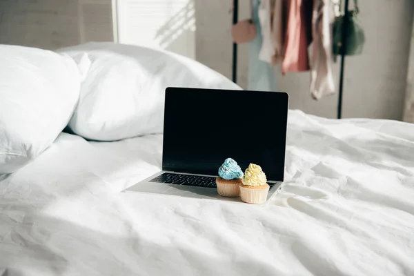 Sweet and tasty cupcakes on laptop with blank screen in bedroom — Stock Photo