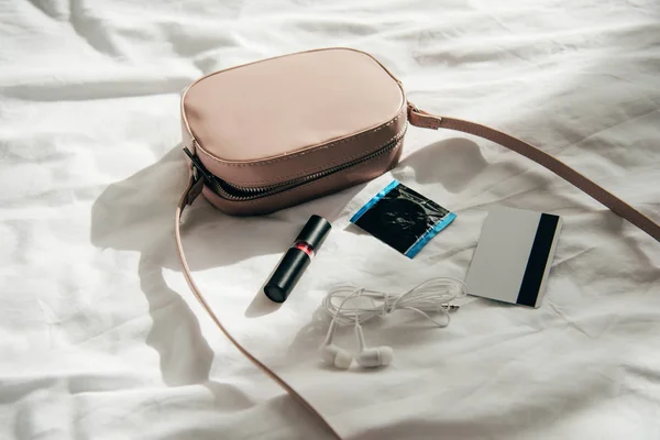 Pink bag near lipstick, earphones, credit card and comdom — Stock Photo