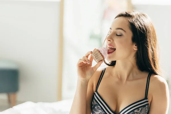 Sexy Frau im BH isst leckere Sahne auf Cupcake — Stockfoto