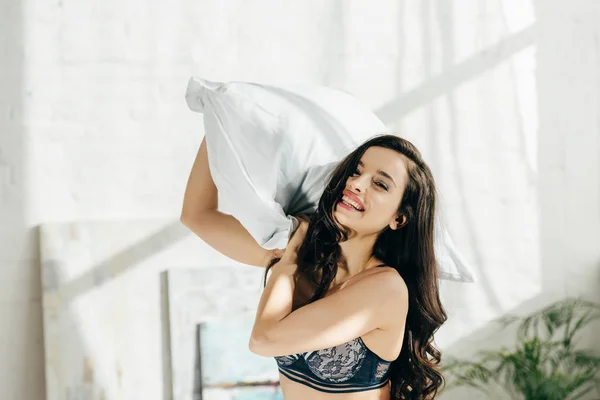 Playful brunette woman in bra holding pillow in hands — Stock Photo