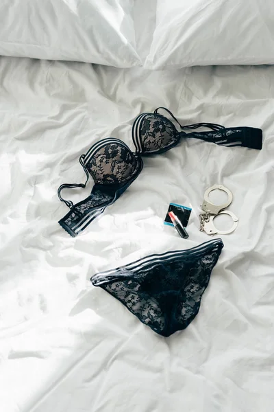 Black lace underwear near condom, handcuffs and condom on bed — Stock Photo