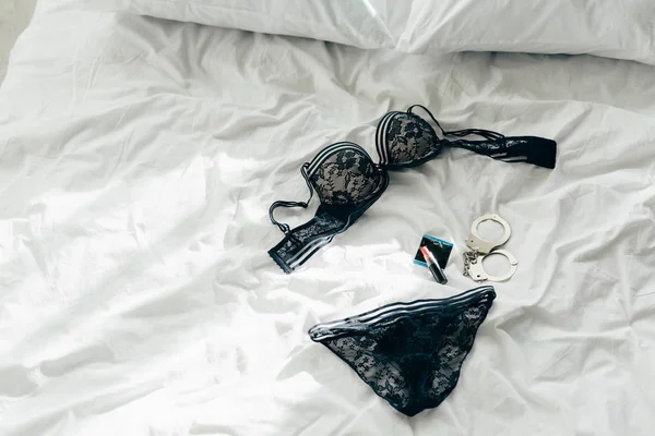 Ropa interior de encaje negro cerca del condón, esposas y condón en la cama - foto de stock