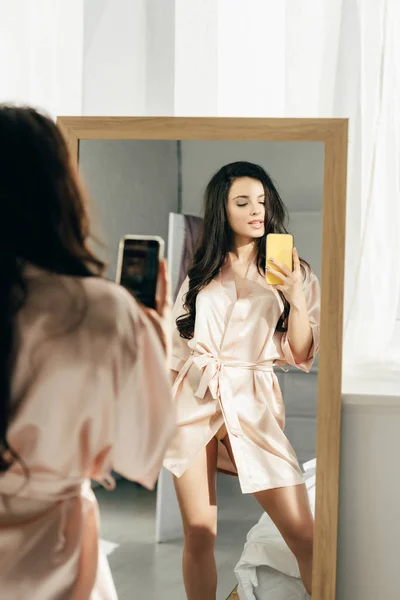 Приваблива брюнетка жінка робить фотографію, стоячи біля дзеркала — стокове фото