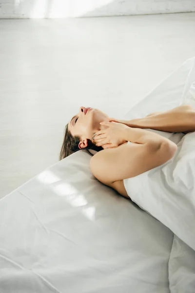 Красива дівчина лежить на ліжку і торкається шиї в сучасній спальні — стокове фото