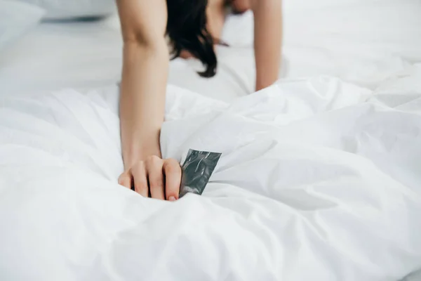 Vista cortada da mulher segurando preservativo na cama branca — Fotografia de Stock