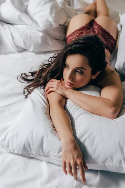 Sexy brunette girl in red panties lying on pillow in bed — Stock Photo