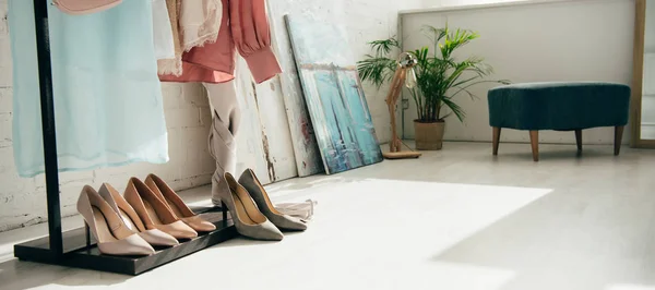 Plano panorámico de ropa de moda cerca de tacones altos y pared de ladrillo blanco - foto de stock