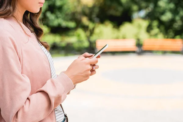 Vista recortada de la niña usando el teléfono inteligente mientras está de pie en el parque - foto de stock