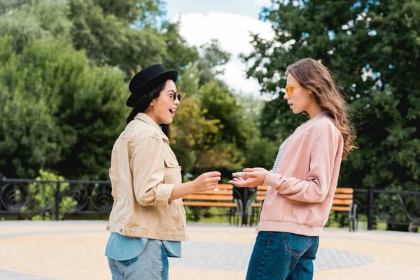 Surpris les filles dans des lunettes de soleil en se regardant dans le parc — Photo de stock