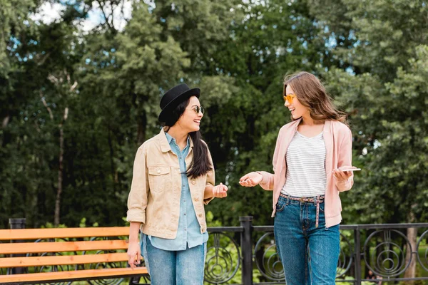 Meninas bonitas em óculos de sol sorrindo enquanto olham um para o outro no parque — Fotografia de Stock