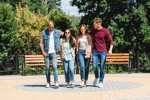 Feliz grupo multicultural de amigos sonriendo mientras caminan en el parque - foto de stock