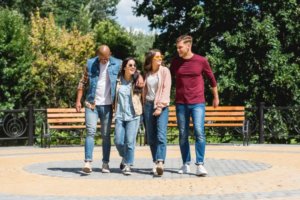 Alegre grupo multicultural de amigos sonriendo mientras caminan en el parque - foto de stock