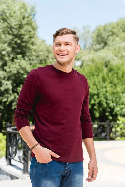 Fröhlicher junger Mann lächelt, während er mit der Hand in der Tasche steht — Stockfoto