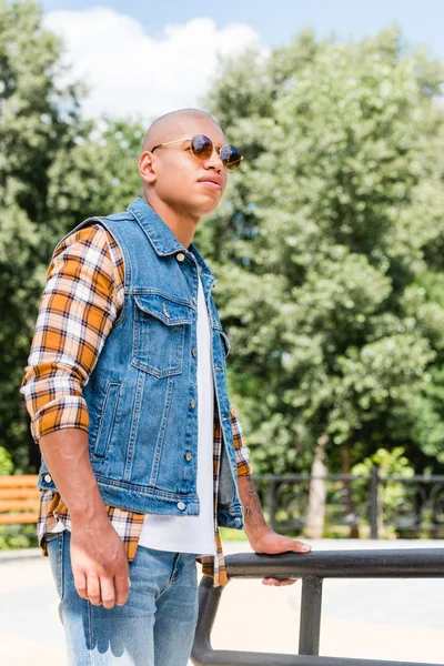 Beau jeune homme afro-américain en lunettes de soleil debout dans le parc — Photo de stock