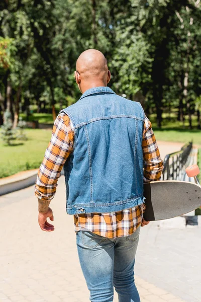 Vue arrière de jeune homme afro-américain tenant longboard dans le parc — Photo de stock