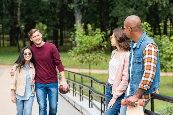 Happy man holding american football and walking with girl near multicultural friends — Stock Photo