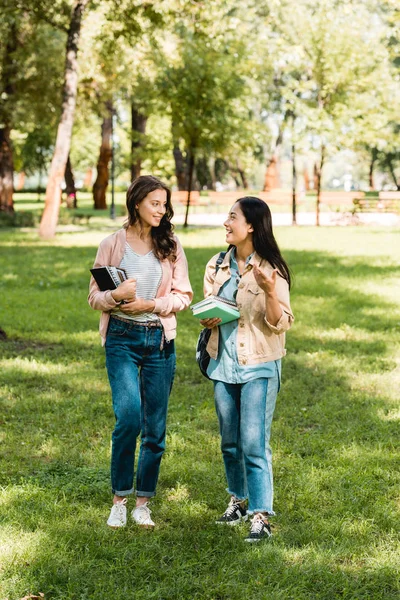 Hübsche Mädchen, die Bücher in der Hand halten und einander beim Reden im Park anschauen — Stockfoto