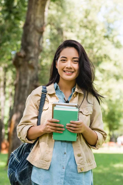 Glückliche junge Frau hält Bücher in der Hand und lächelt im Park — Stockfoto