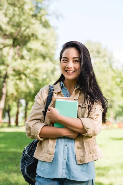 Bella giovane donna che tiene libri e sorride nel parco — Foto stock