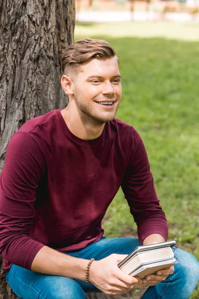 Allegro studente che tiene libri e sorride nel parco — Foto stock