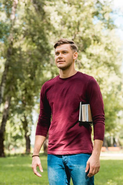 Schöne Studentin steht mit Büchern im Park und lächelt — Stockfoto