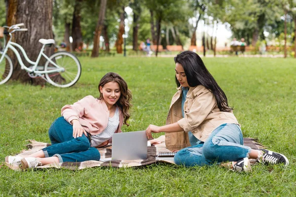 Hermosas chicas mirando a la computadora portátil durante el picnic en el parque - foto de stock