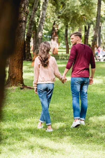 Enfoque selectivo del hombre guapo cogido de la mano con la novia en el parque - foto de stock