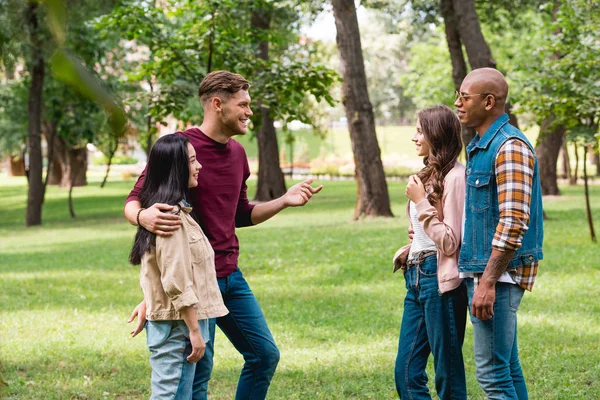 Cheerful multicultural friends talking while standing in park — Stock Photo