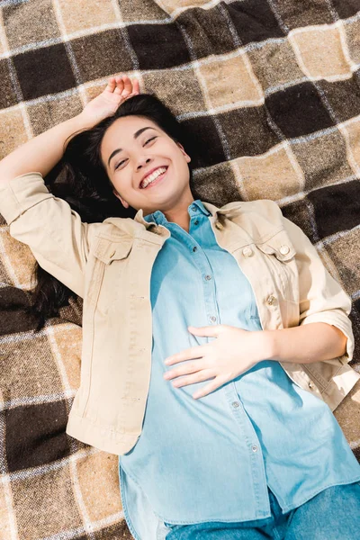 Vue aérienne de fille heureuse souriant tout en étant couché sur une couverture à carreaux — Photo de stock