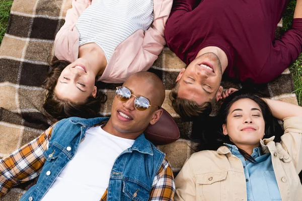 Overhead view of happy multicultural friends lying on checkered blanket — Stock Photo