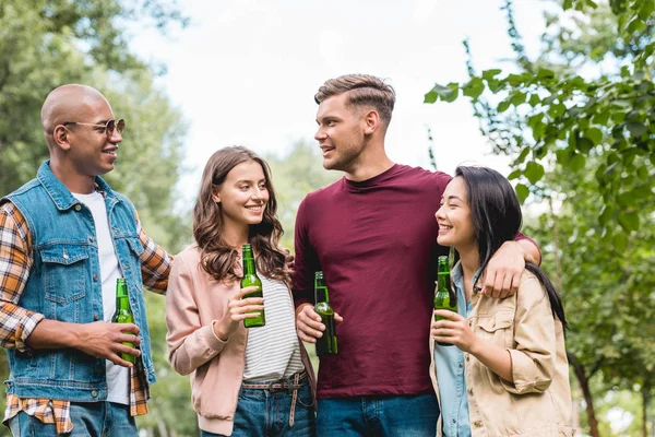 Allegro gruppo multiculturale di amici che tengono bottiglie con birra e parlano nel parco — Foto stock