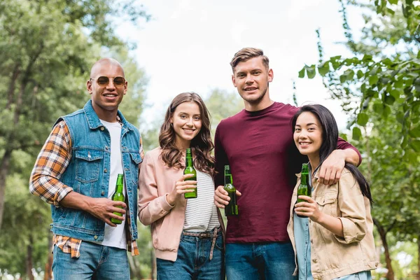 Fröhliche multikulturelle Gruppe von Freunden, die Flaschen mit Bier in der Hand halten und in die Kamera schauen — Stockfoto