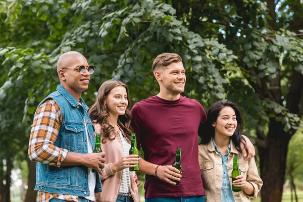 Grupo multiétnico feliz de amigos segurando garrafas com cerveja no parque — Fotografia de Stock