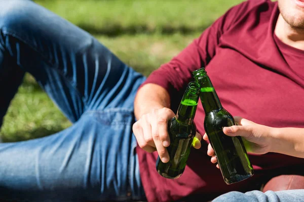 Vista ritagliata di coppia bottiglie di tostatura con birra mentre sdraiato nel parco — Foto stock