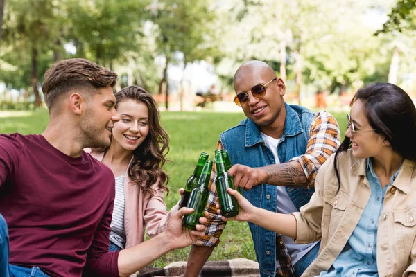 Alegre grupo multiétnico de amigos tintineo botellas de cerveza en el parque - foto de stock