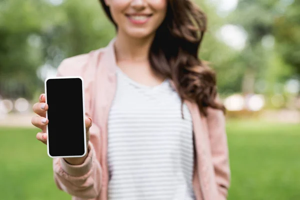 Enfoque selectivo de niña alegre sosteniendo teléfono inteligente con pantalla en blanco - foto de stock