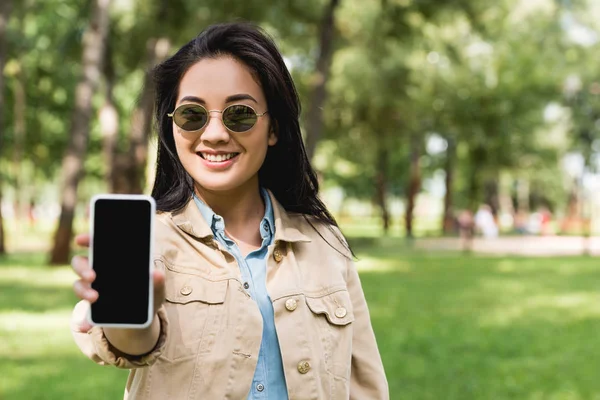 Messa a fuoco selettiva della ragazza allegra in occhiali da sole con smartphone con schermo bianco — Foto stock