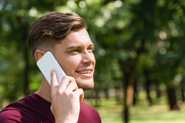 Cheerful young man talking on smartphone in park — Stock Photo