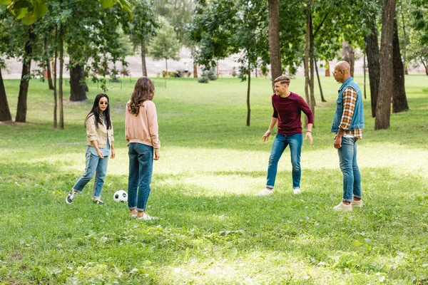 Alegre grupo multiétnico de amigos jugando al fútbol en el parque - foto de stock