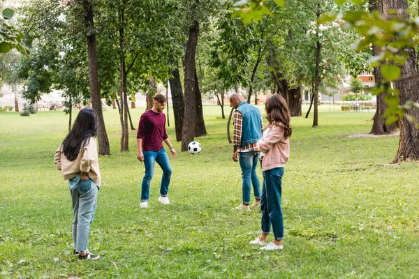 Cheerful multicultural group of friends standing in park near football — Stock Photo