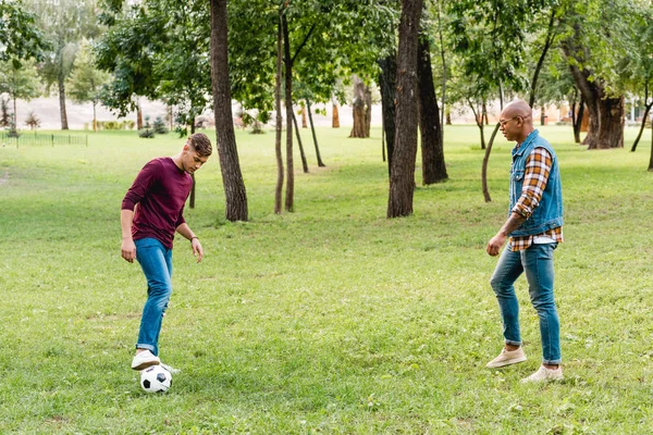Amigos multiculturales jugando al fútbol sobre hierba verde en el parque - foto de stock