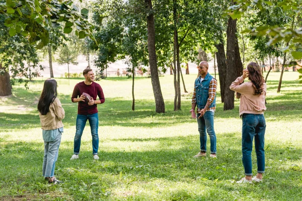 Happy multicultural group of friends playing american football in park — Stock Photo