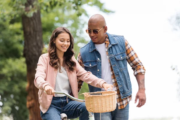 Happy african american man looking at pretty girlfriend riding bicycle — Stock Photo