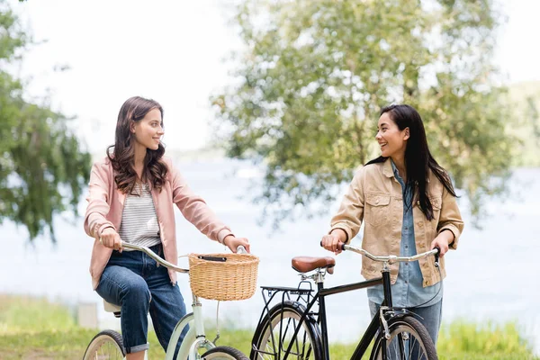 Chicas alegres montando bicicletas y sonriendo en el parque - foto de stock