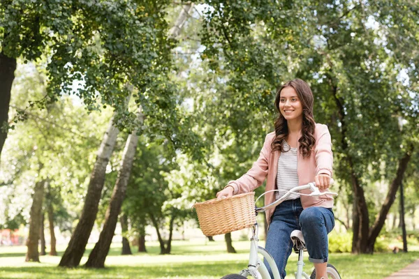 Happy pretty young woman riding bicycle in park — Stock Photo