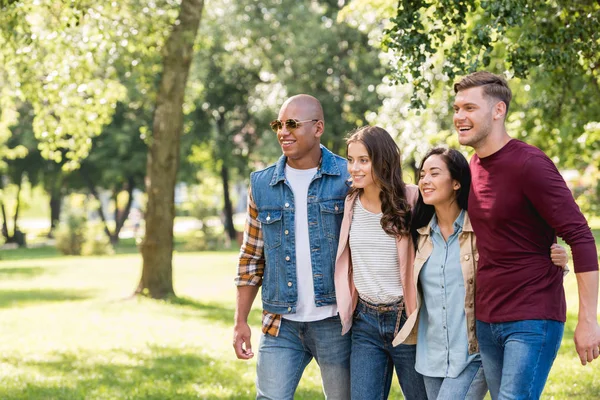 Cheerful multiethnic friends hugging while walking together in park — Stock Photo